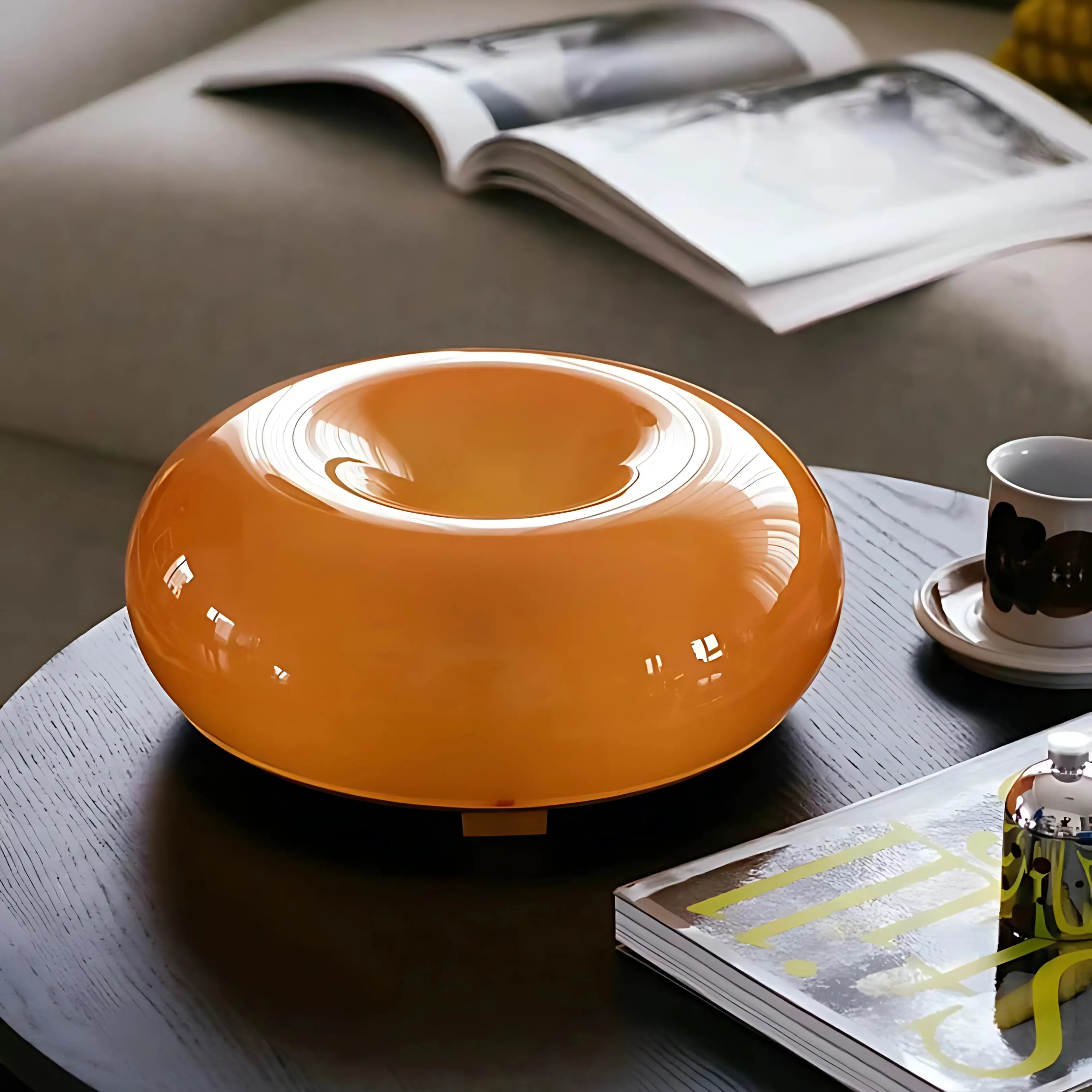 Sole Ambrato glossy amber donut lamp on a table with a book
