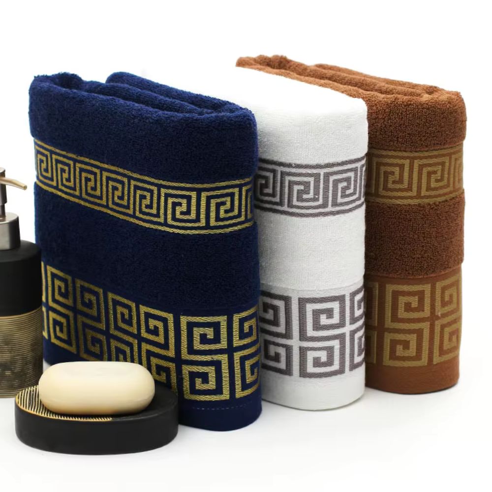 Navy, white and bronze Greek key cotton towels rolled beside a soap dish