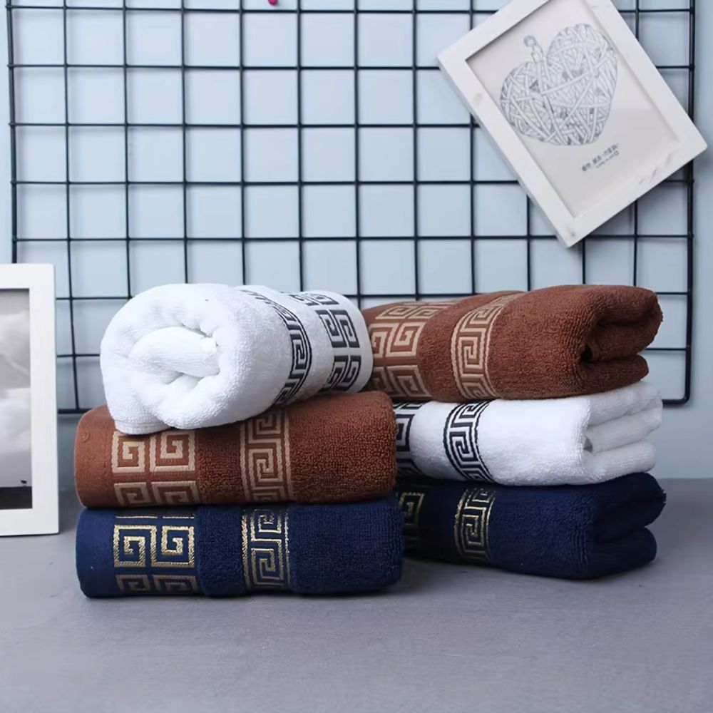 Folded white, bronze and navy Greek key cotton towels styled with framed art