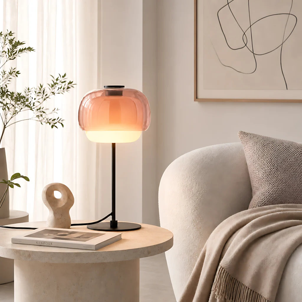 Blush double-dome glass table lamp on a stone side table next to a curved armchair