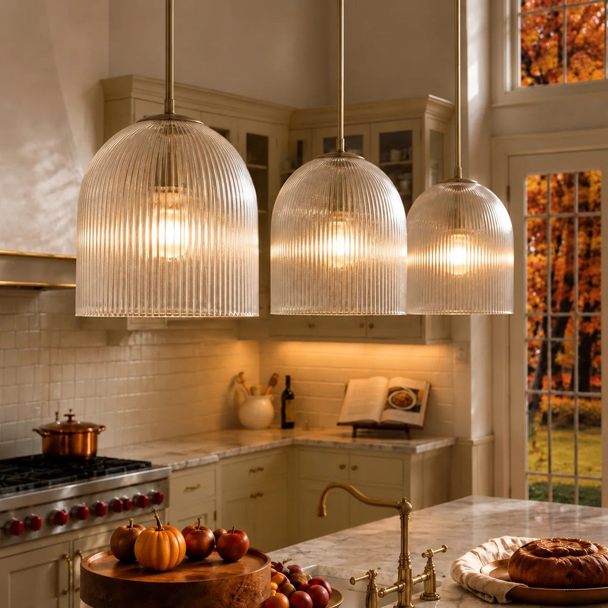 Three brass ribbed glass dome pendants glowing over a marble kitchen island