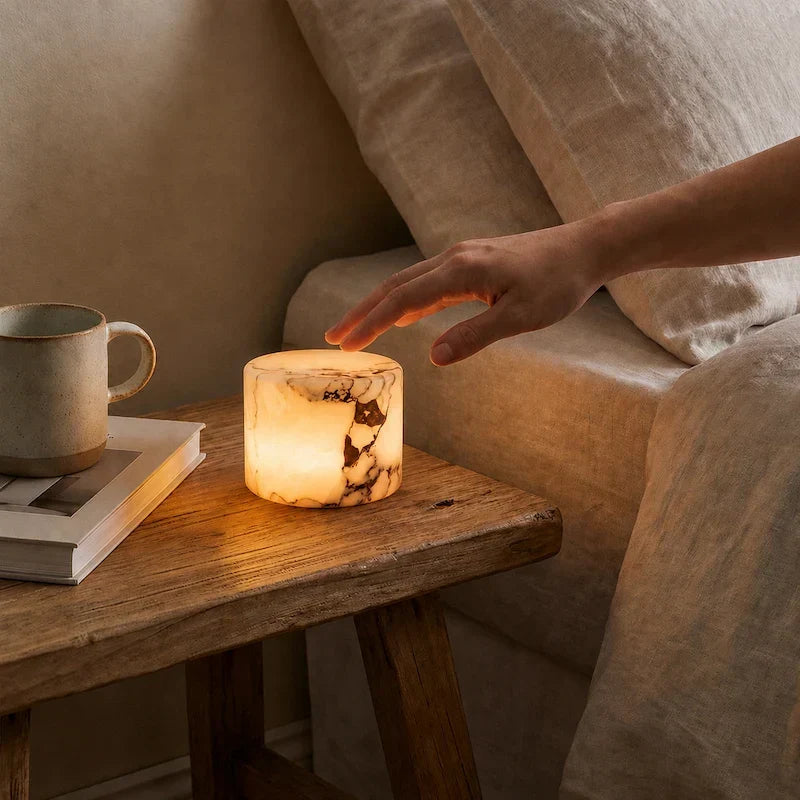Hand touching the Pietra Lunare marble touch lamp on a rustic bedside bench
