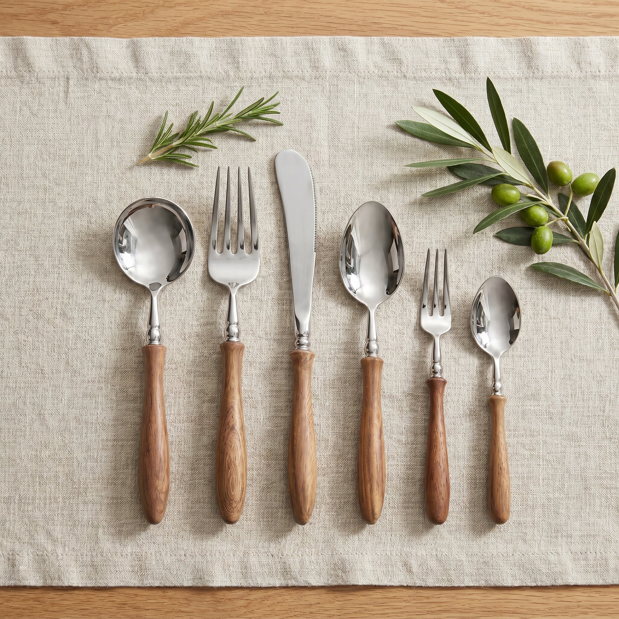 Top-down flat-lay of the complete six-piece Bosco Rustico wood-handle flatware set on linen with rosemary and olive