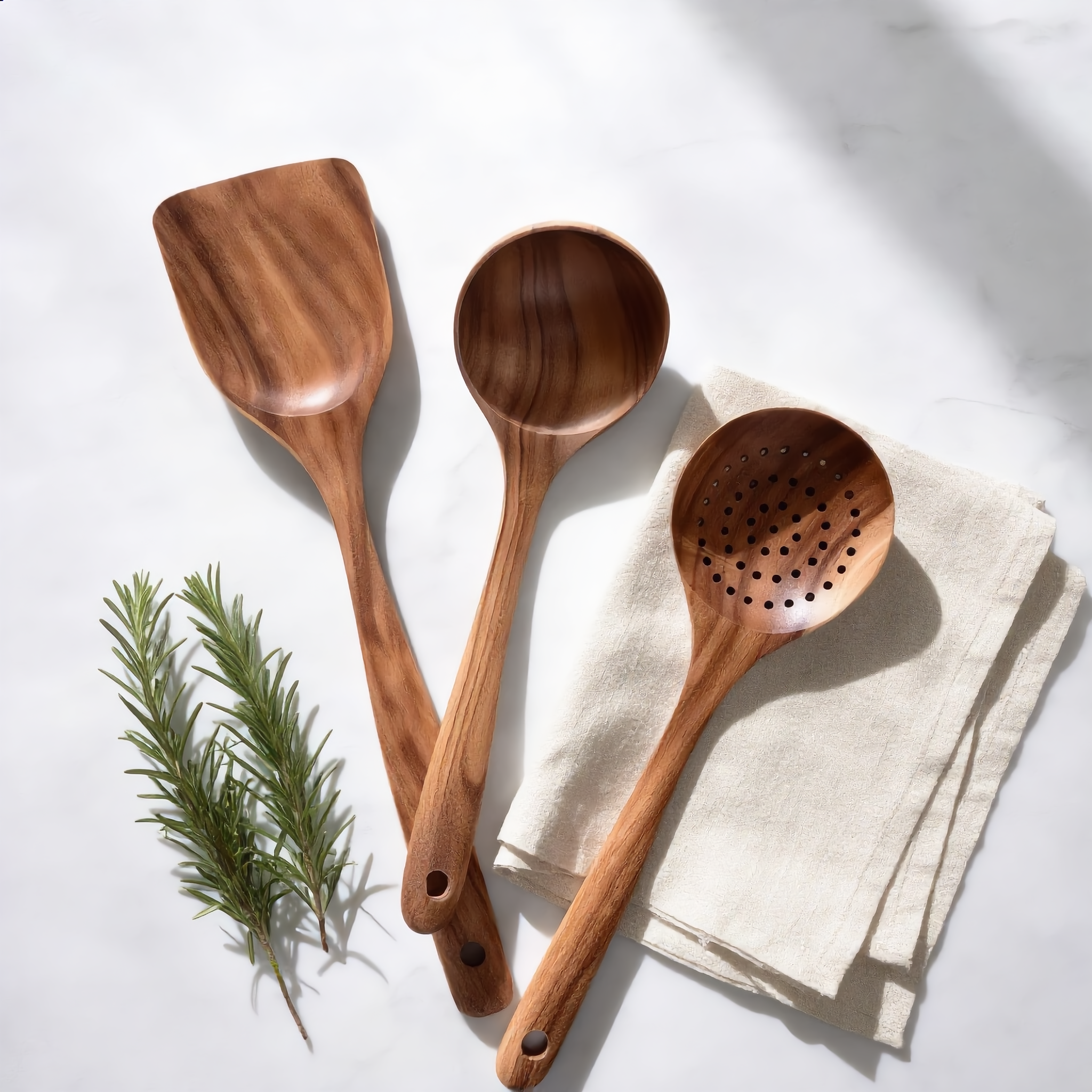 Teak turner, spoon and slotted skimmer on marble with rosemary