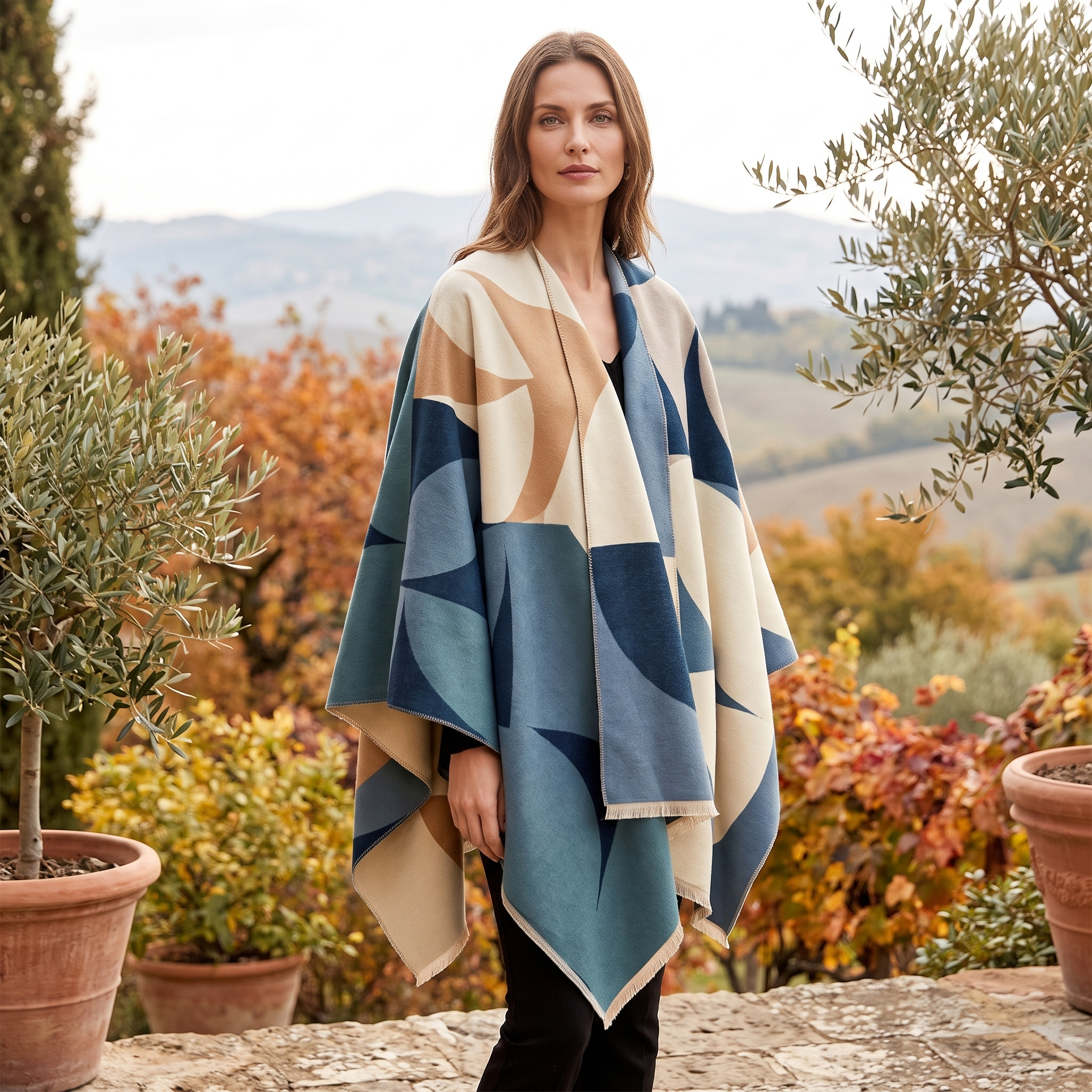 Woman wearing teal blue geometric reversible wrap poncho on a countryside terrace