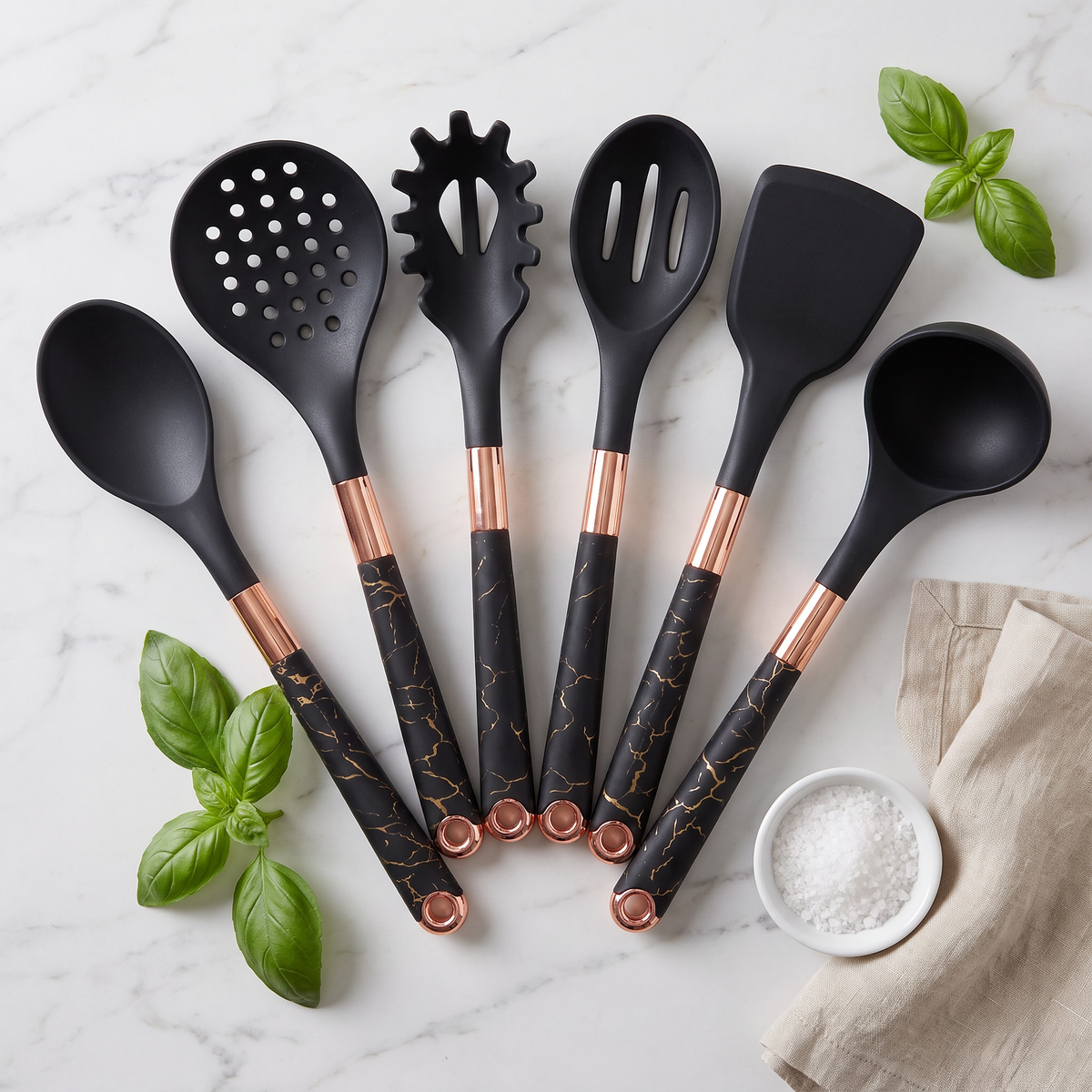 Flat lay of the six black Marmo crackle-marble utensils with rose-gold collars on marble with basil