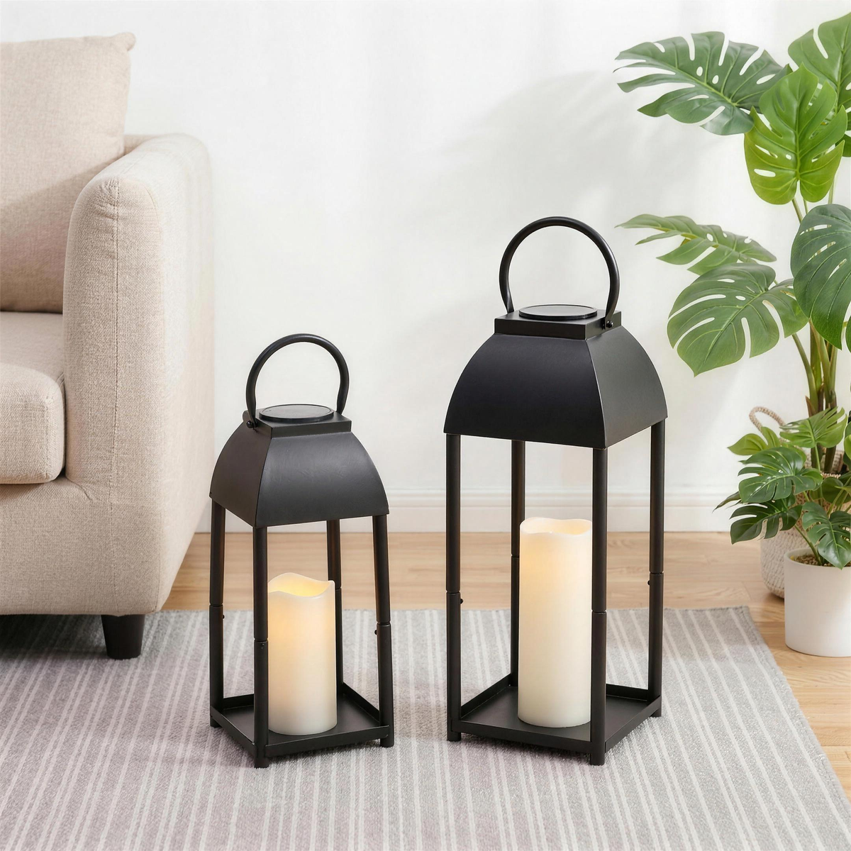Pair of black lanterns beside a cream sofa and monstera plant