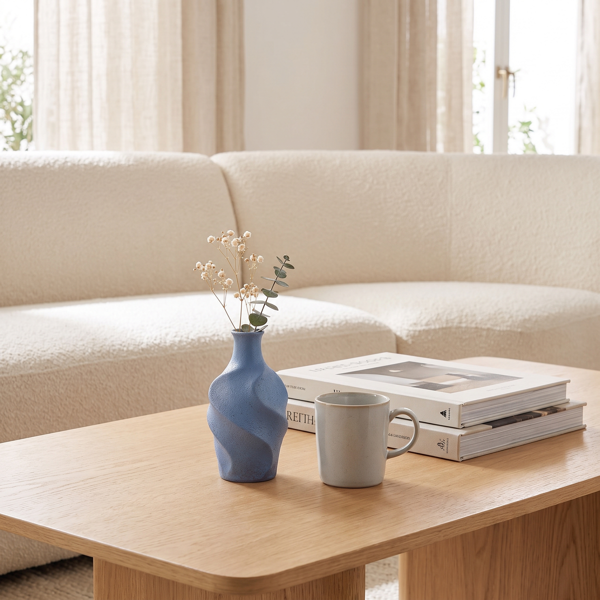 Virella Sculpt small blue twisted bud vase with dried baby's breath beside a coffee mug on an oak coffee table