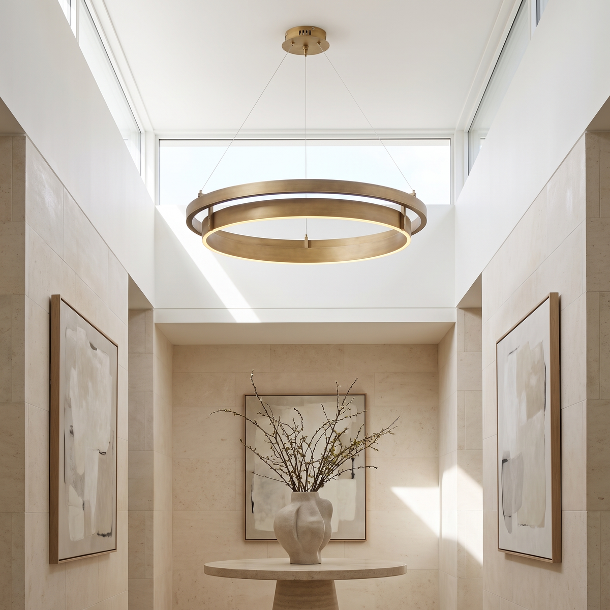 View from below of the two overlapping brushed brass rings of the chandelier in a bright gallery hall