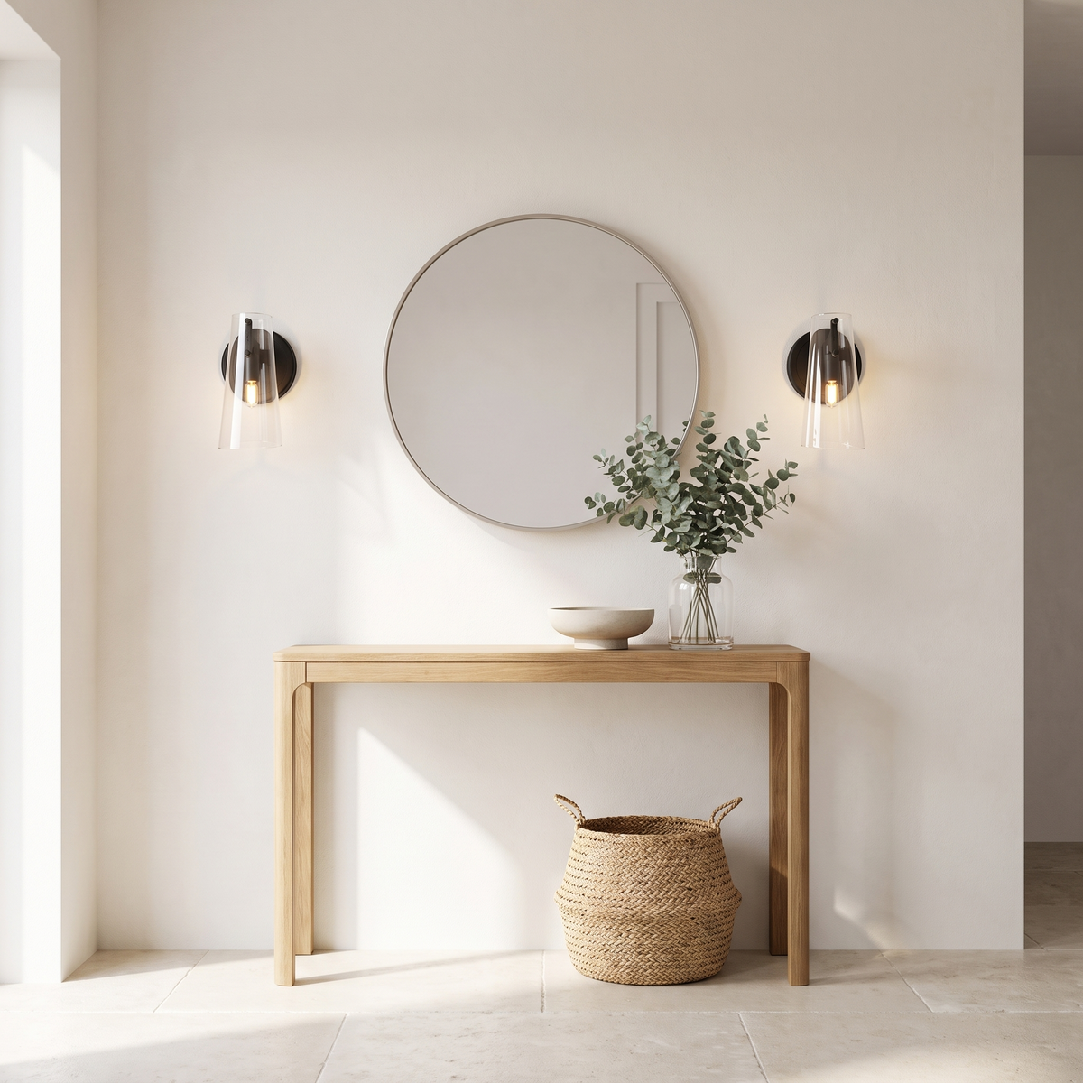 Pair of glass cone wall sconces either side of a round mirror above an oak console in a bright entryway
