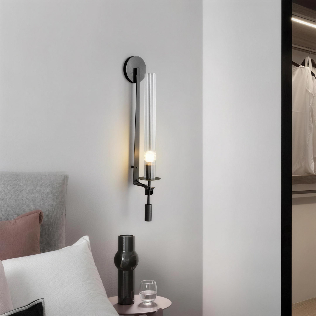 Black ribbed glass wall sconce glowing beside a bed