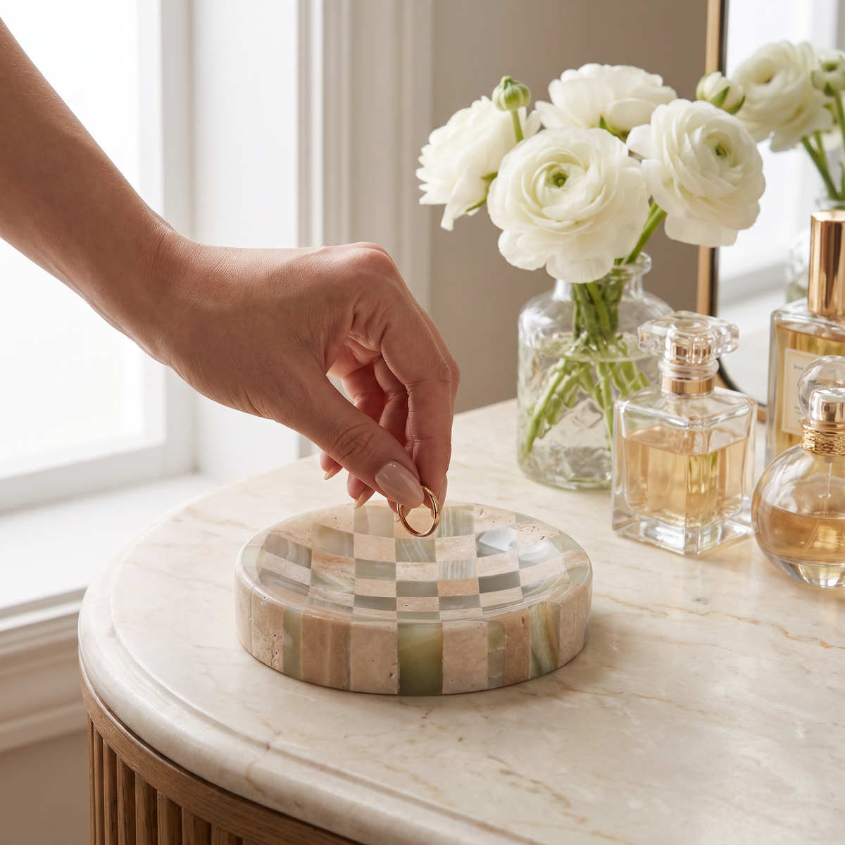 Hand placing a gold ring in the Olvera checkered travertine and onyx trinket dish on a dressing table