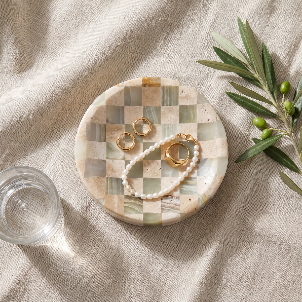 Overhead view of the Olvera checkered dish with gold jewelry on linen