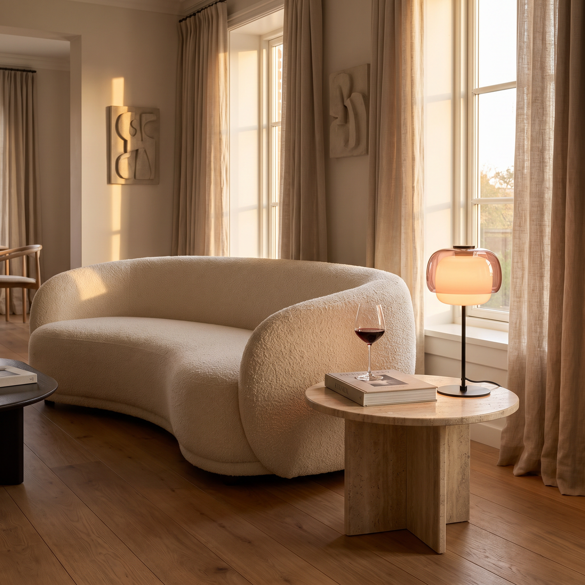 Blush double-dome glass table lamp on a travertine side table beside a curved bouclé sofa