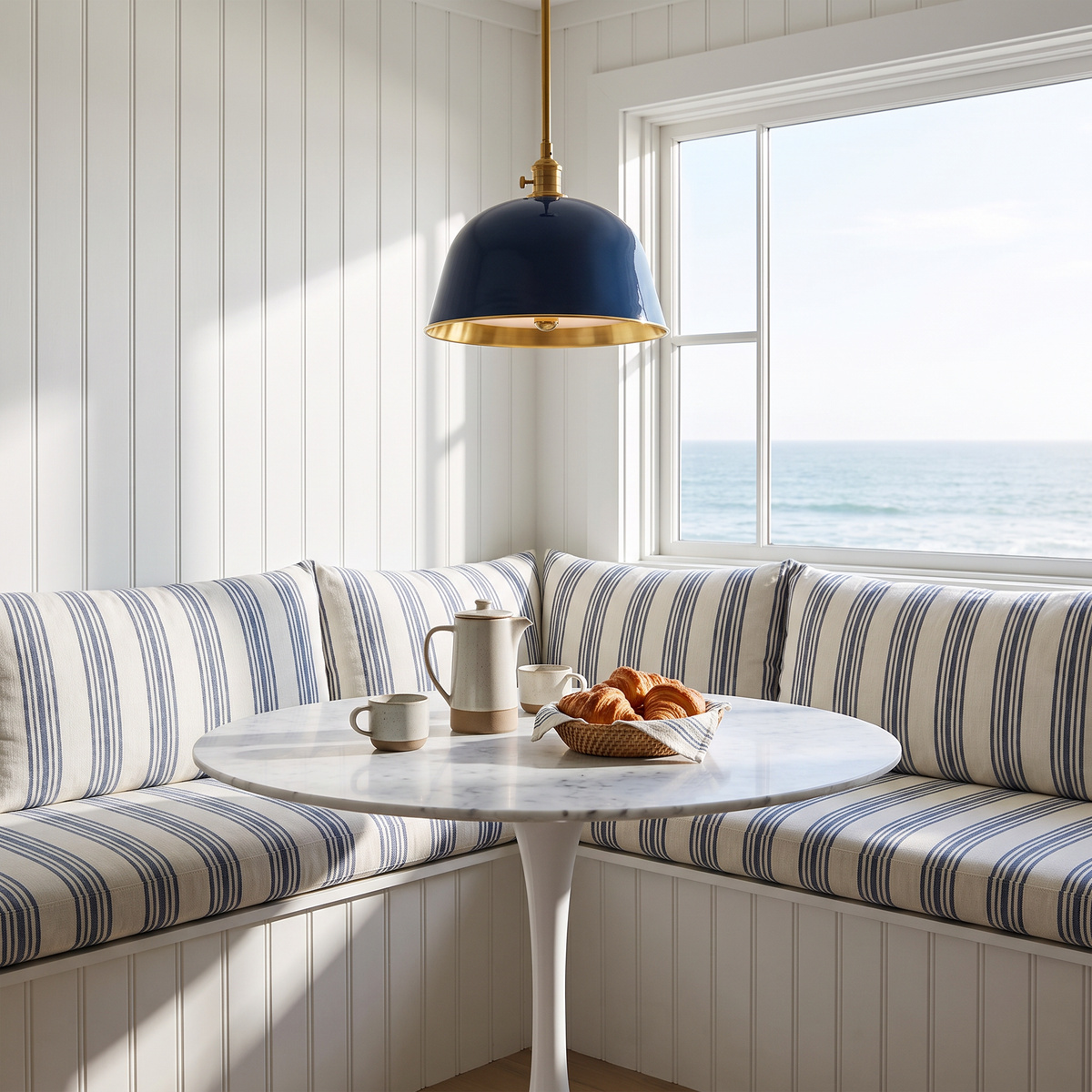 Blue brass-lined bell pendant above a marble table in a coastal breakfast nook