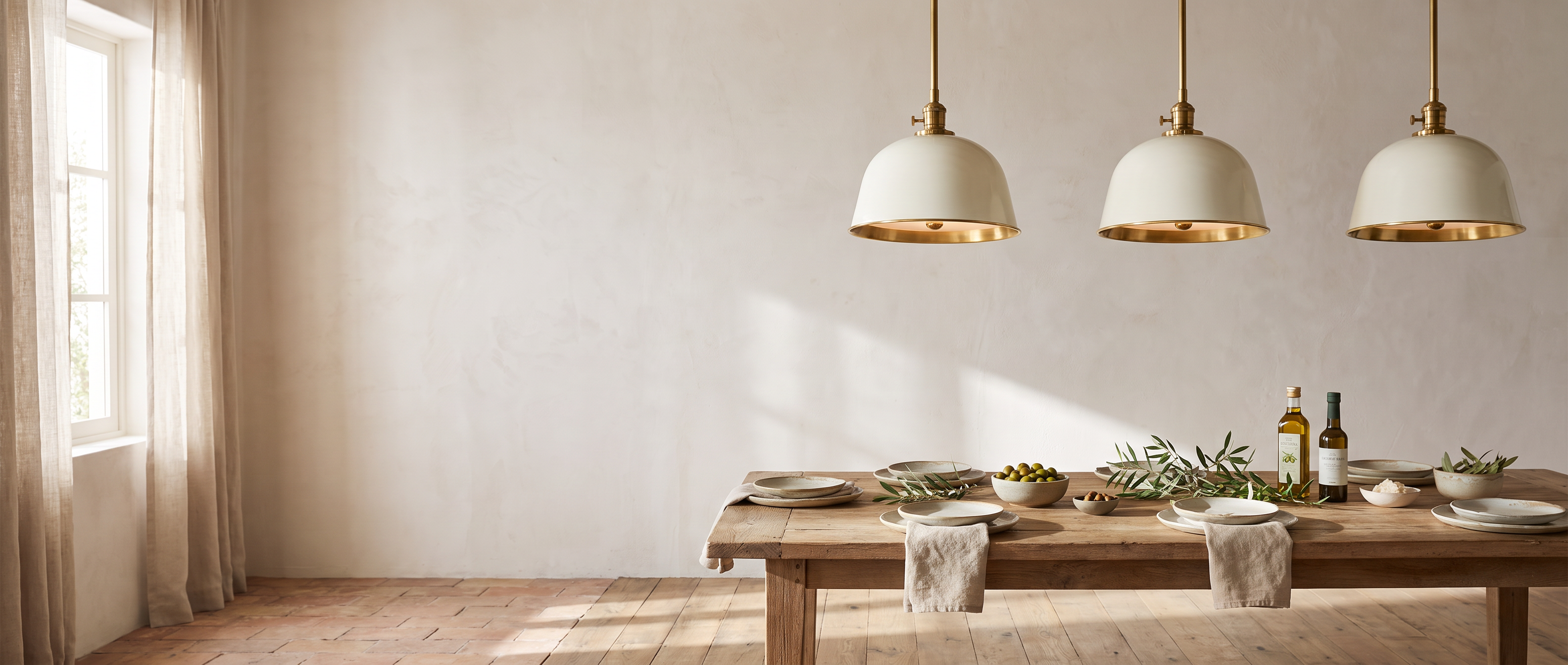 Three white brass-lined bell pendants above a rustic oak table in a sunlit Italian farmhouse dining room