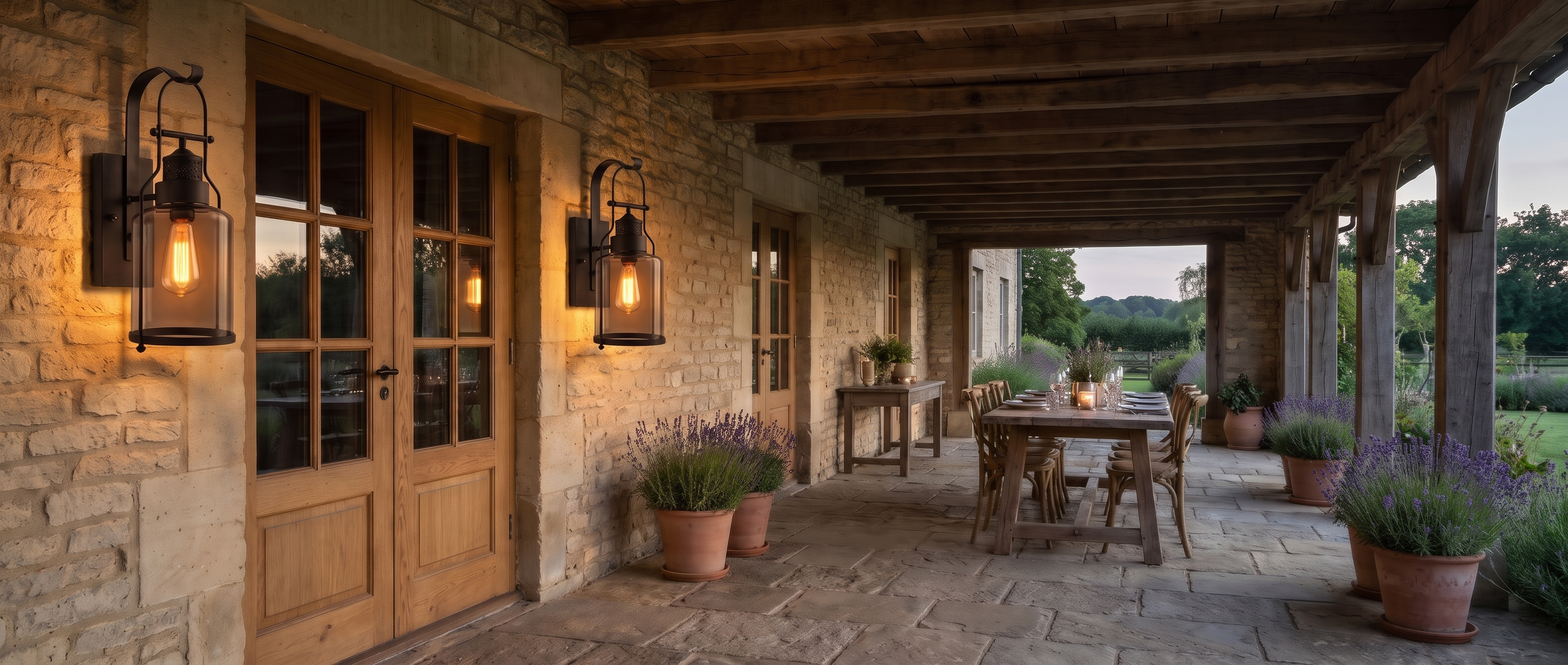 Pair of black lantern wall sconces flanking oak French doors on a stone terrace at dusk