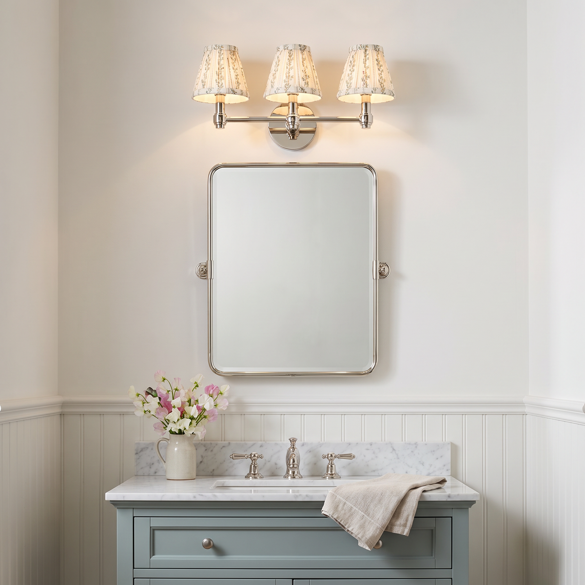 Terzetto polished nickel vanity sconce with floral print shades above a mirror and sage blue vanity