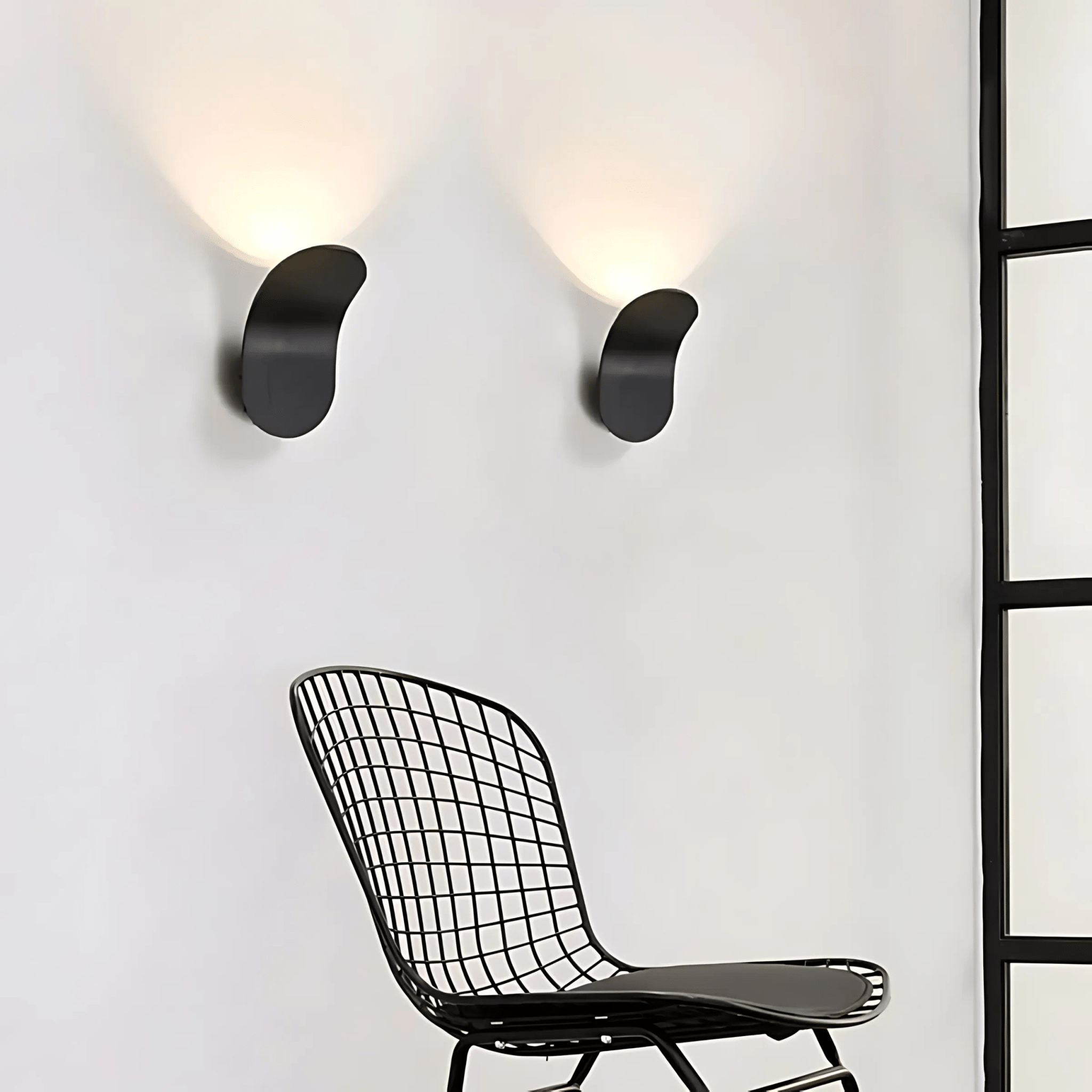 Black curved wall sconces flanking a wire chair