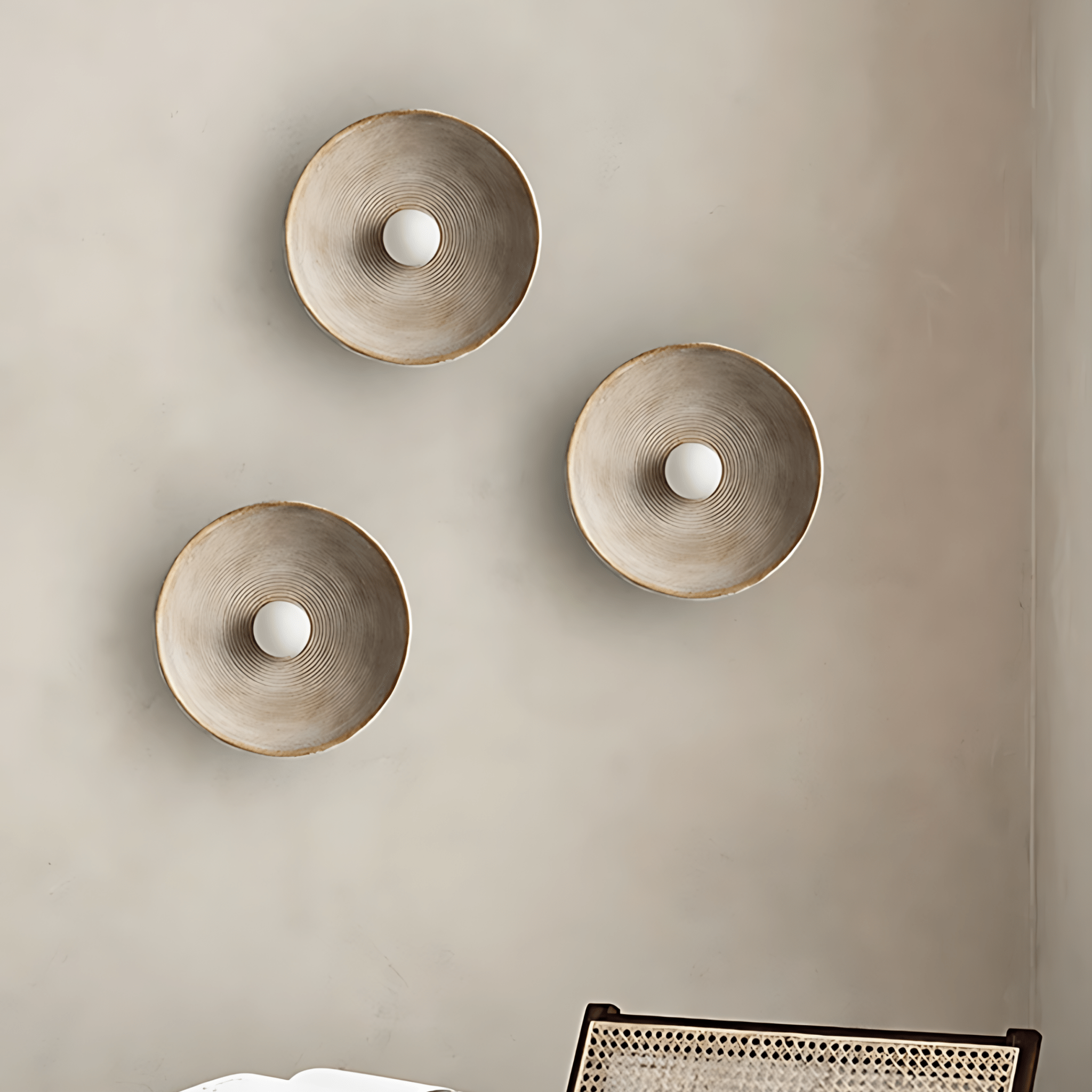 Three Aurelia Sculptural Wall Sconces arranged on a plaster wall above a rattan chair