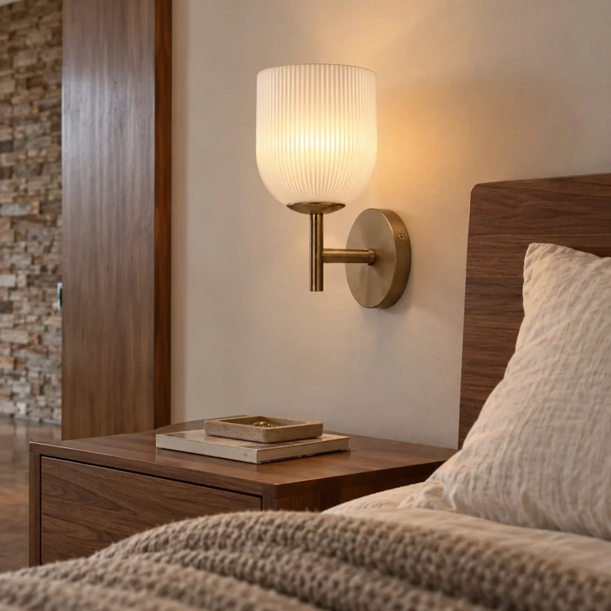 Brass ribbed glass wall sconce above a walnut nightstand in a warm bedroom