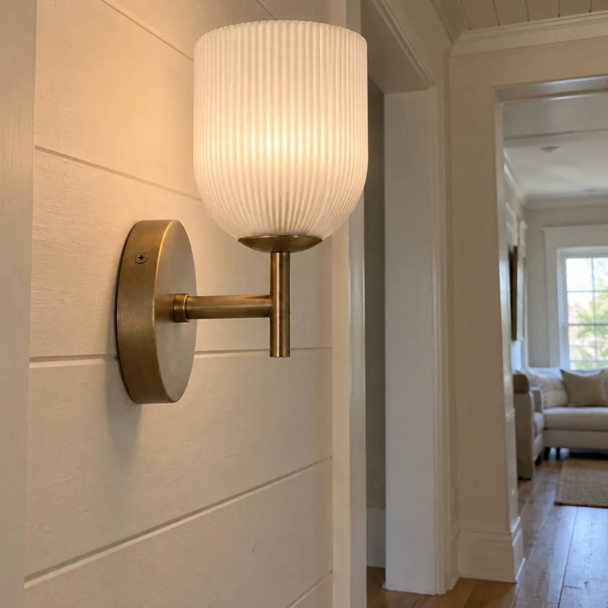 Brass ribbed glass wall sconce on a shiplap wall in a bright hallway
