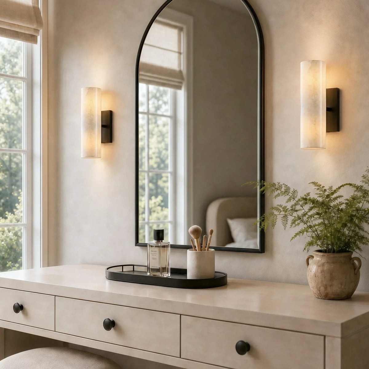Pair of alabaster tube sconces flanking an arched vanity mirror