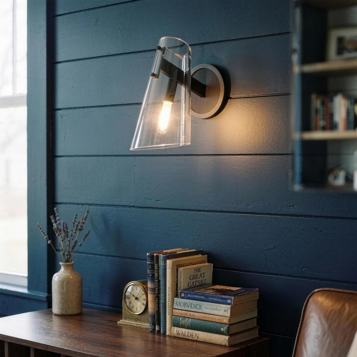 Glass cone wall sconce on a navy shiplap wall above a desk with books