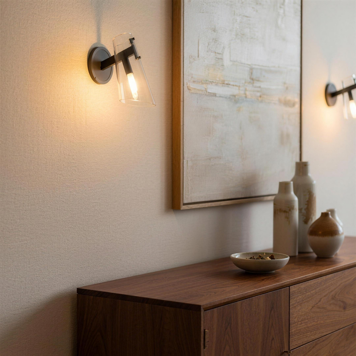 Glass wall sconces above a walnut sideboard beside abstract art