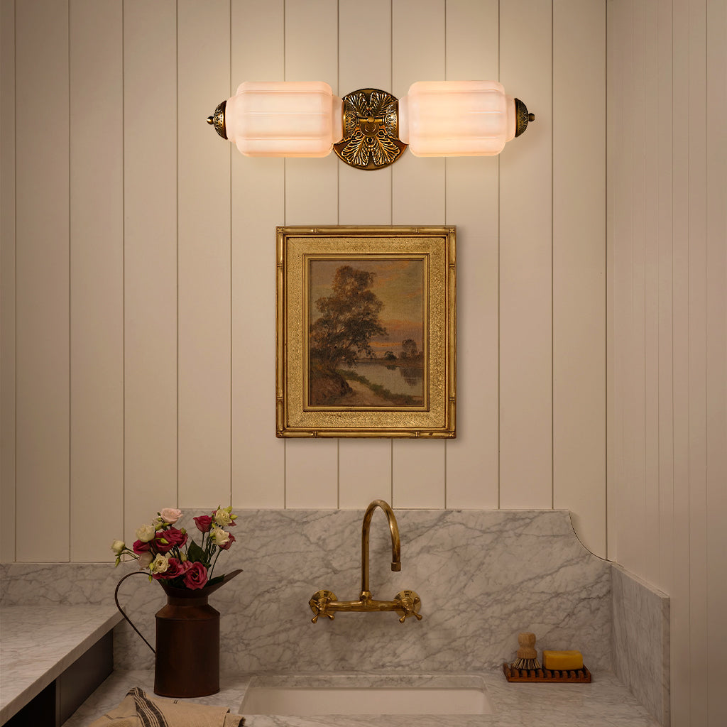 Raggiera Deco vanity light with white glass and brass sunburst plate glowing above a marble sink