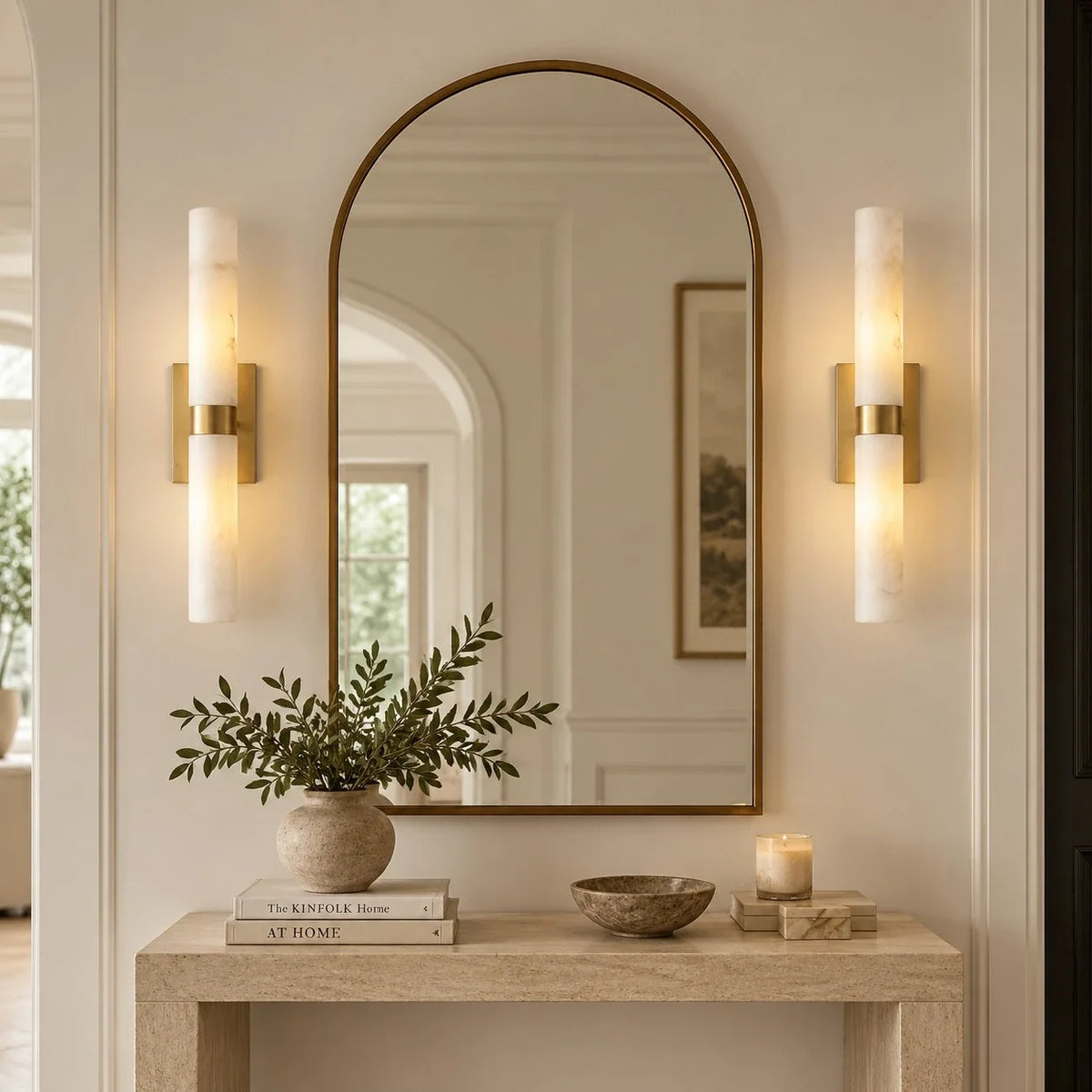 Pair of Stelo Alabastro sconces in tumbled brass flanking an arched mirror above a console