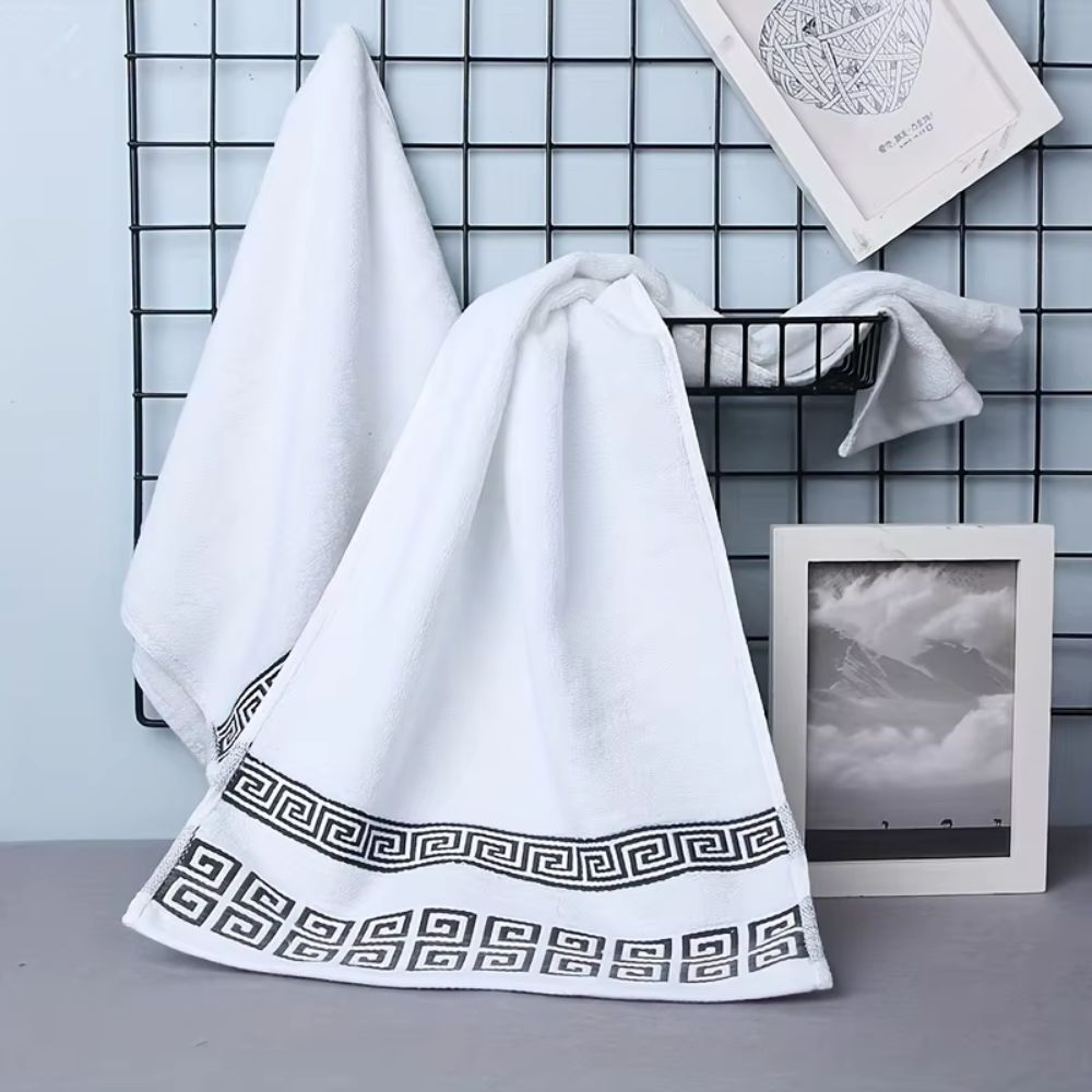 White Greek key cotton bath towels hanging on a wall grid