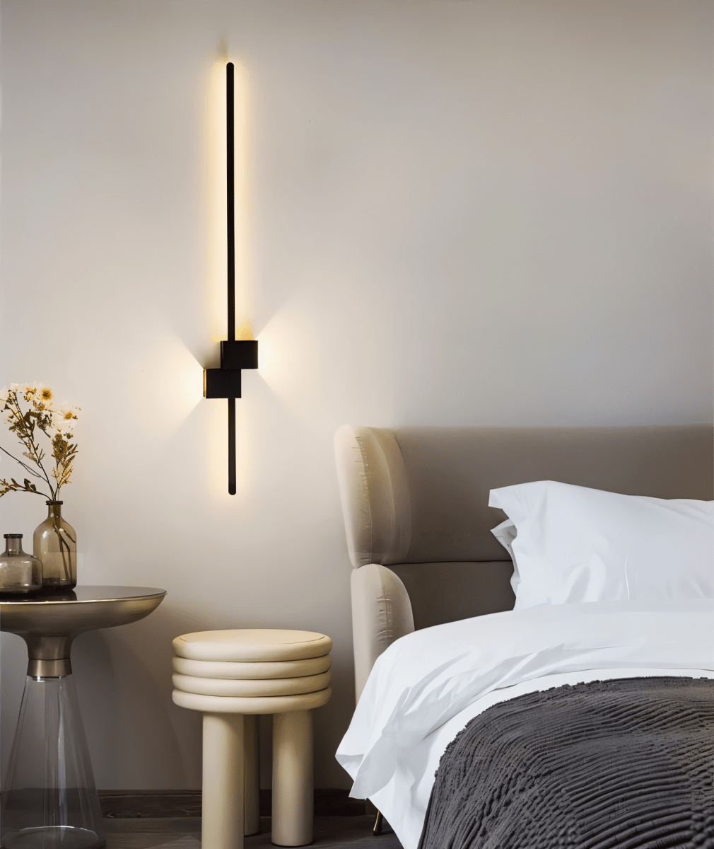 Black linear LED wall light mounted vertically beside a bed, warm glow