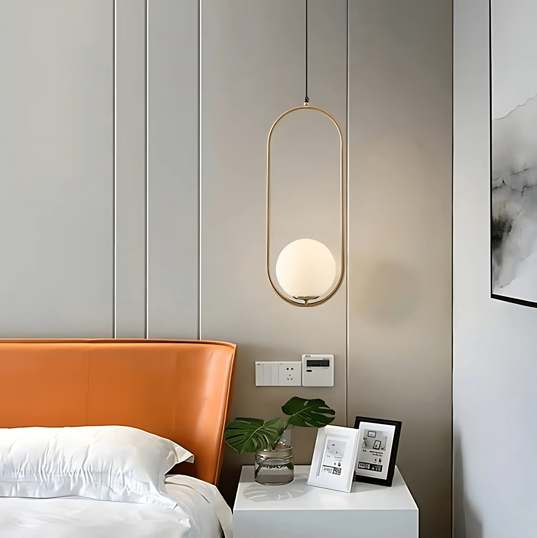 A gold Sfera oval glass-globe pendant beside a bed as a bedside light