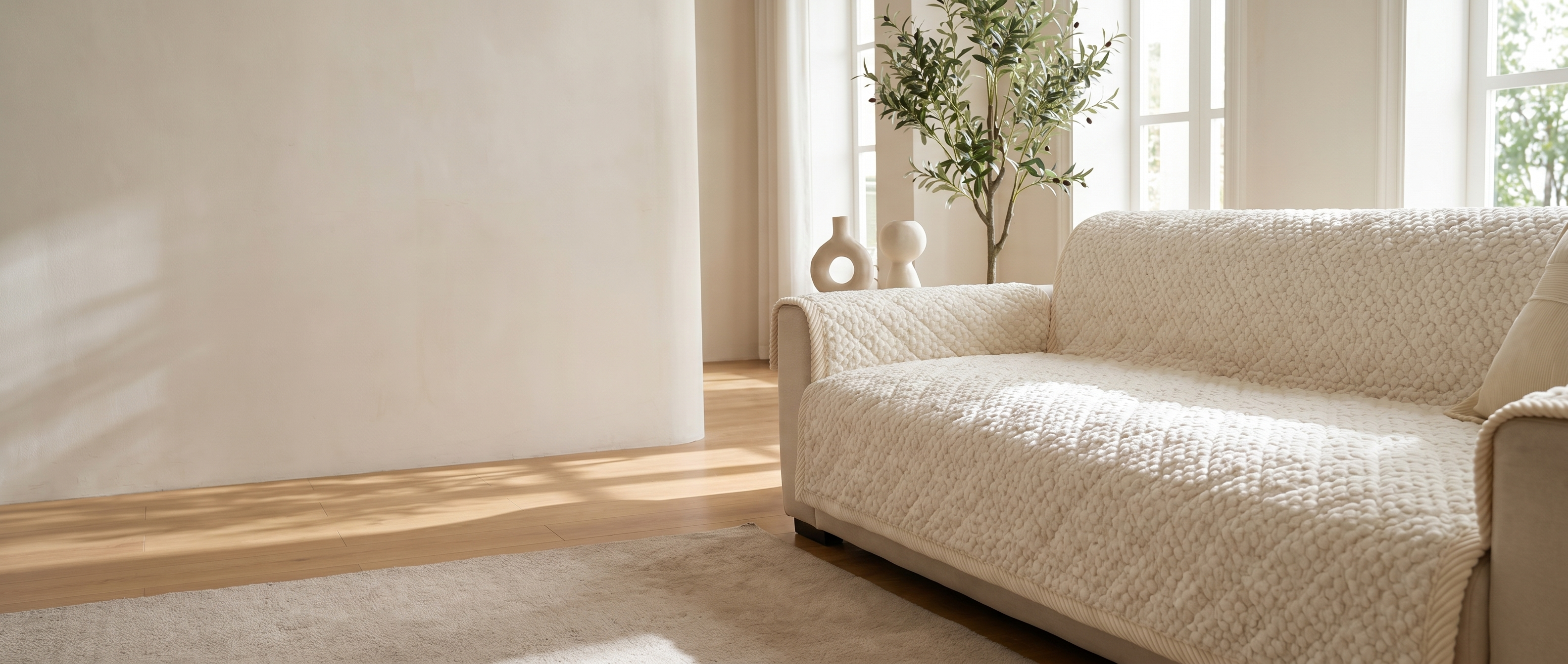 Ivory quilted sofa protector on a sofa in a sunlit modern living room — widescreen banner