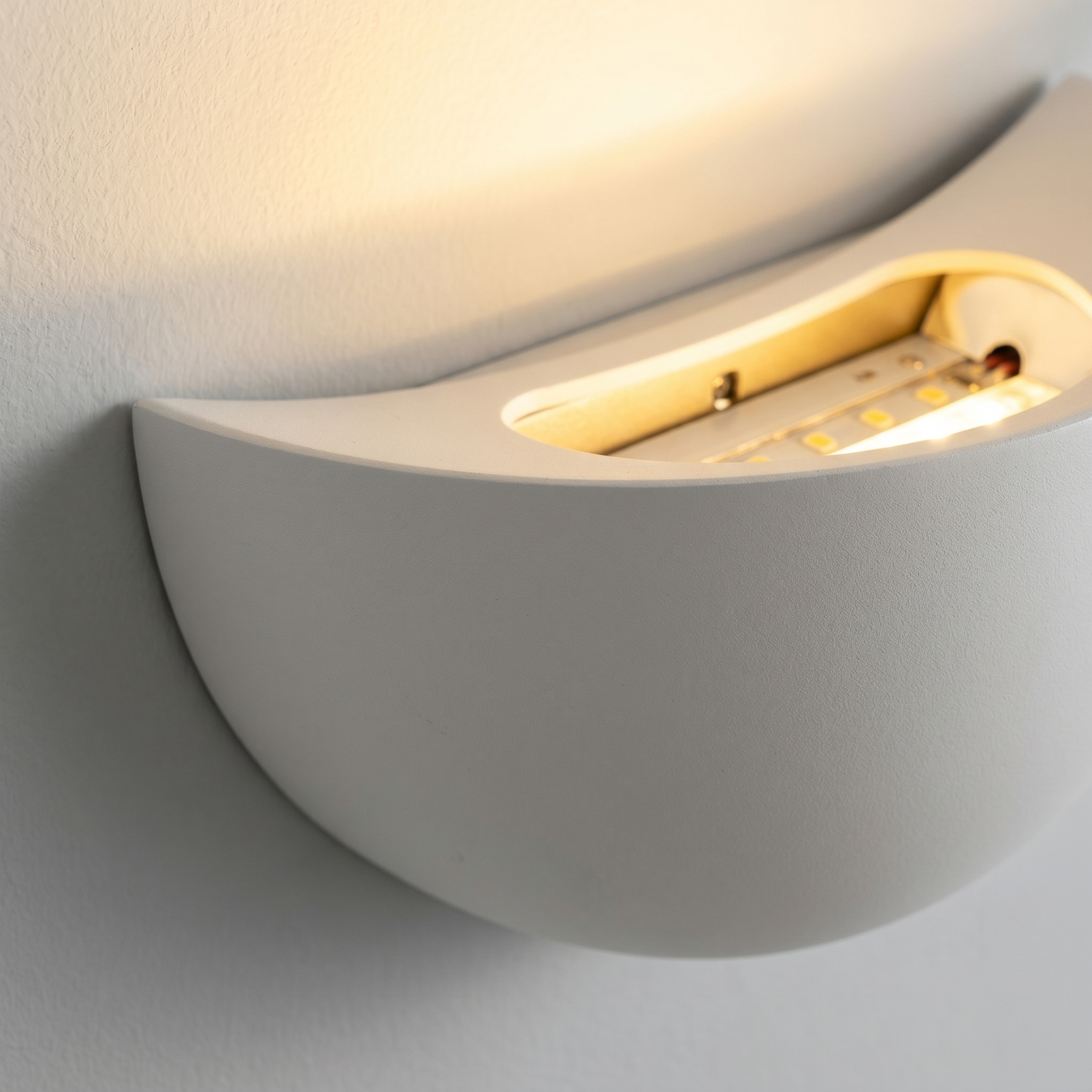 Close-up detail of the white Mezzaluna half-moon wall sconce and its warm emission
