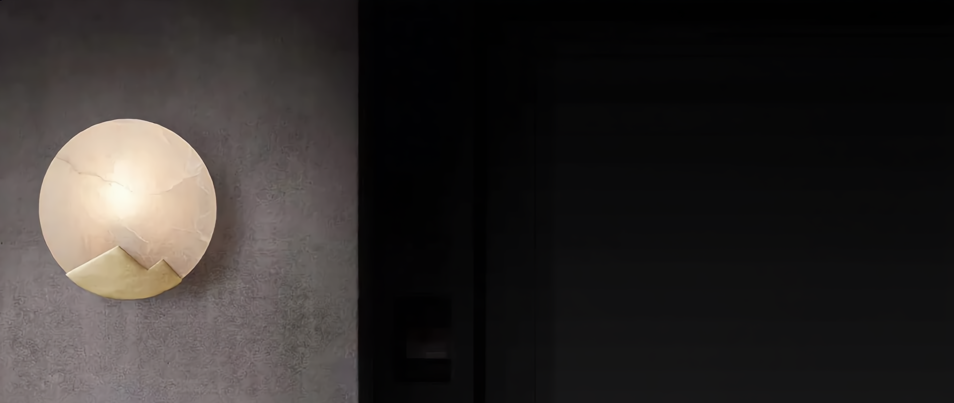 Luna d'Alabastro alabaster moon wall sconce glowing warm on a moody plaster feature wall (banner)