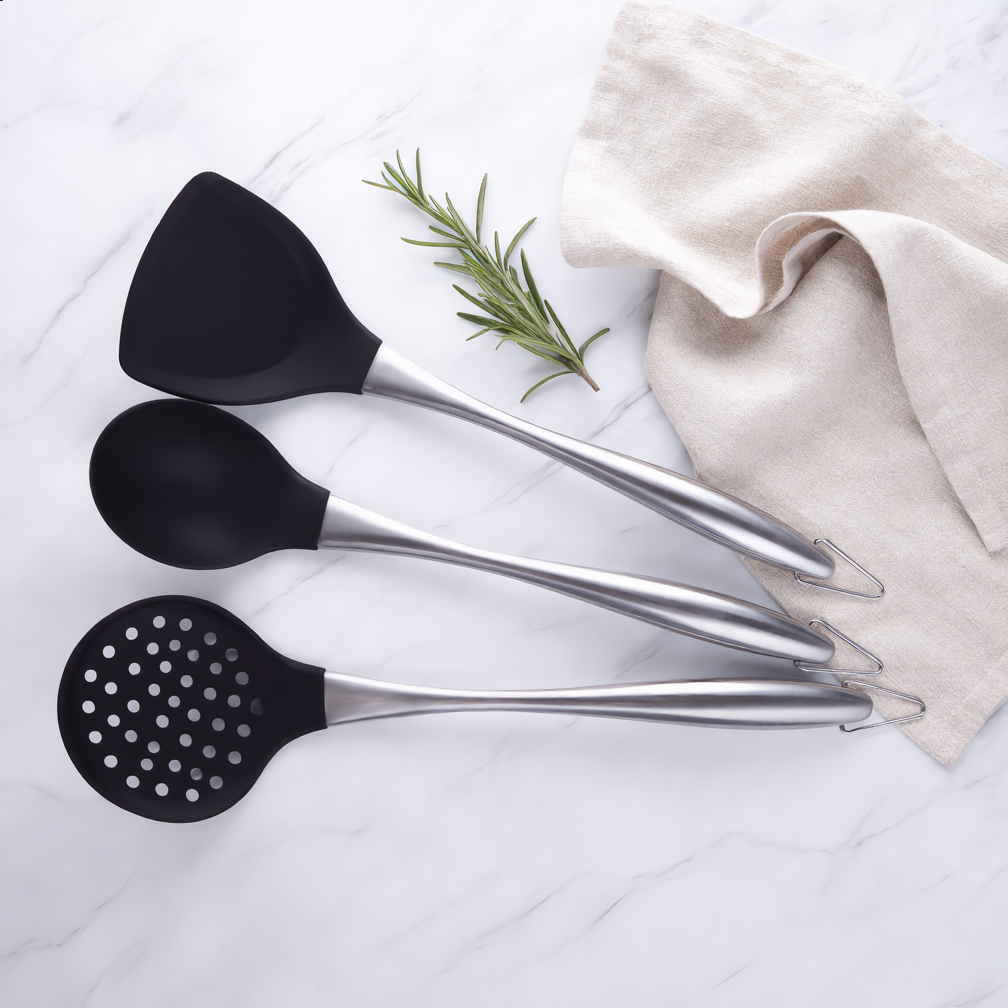 Silver Lustro turner, ladle and slotted skimmer flat-lay on marble with rosemary