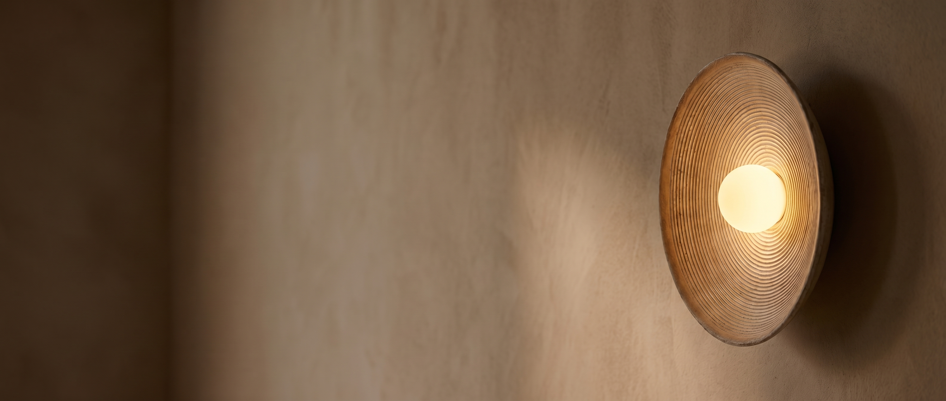 Aurelia Sculptural Wall Sconce glowing warmly on a textured plaster wall at dusk