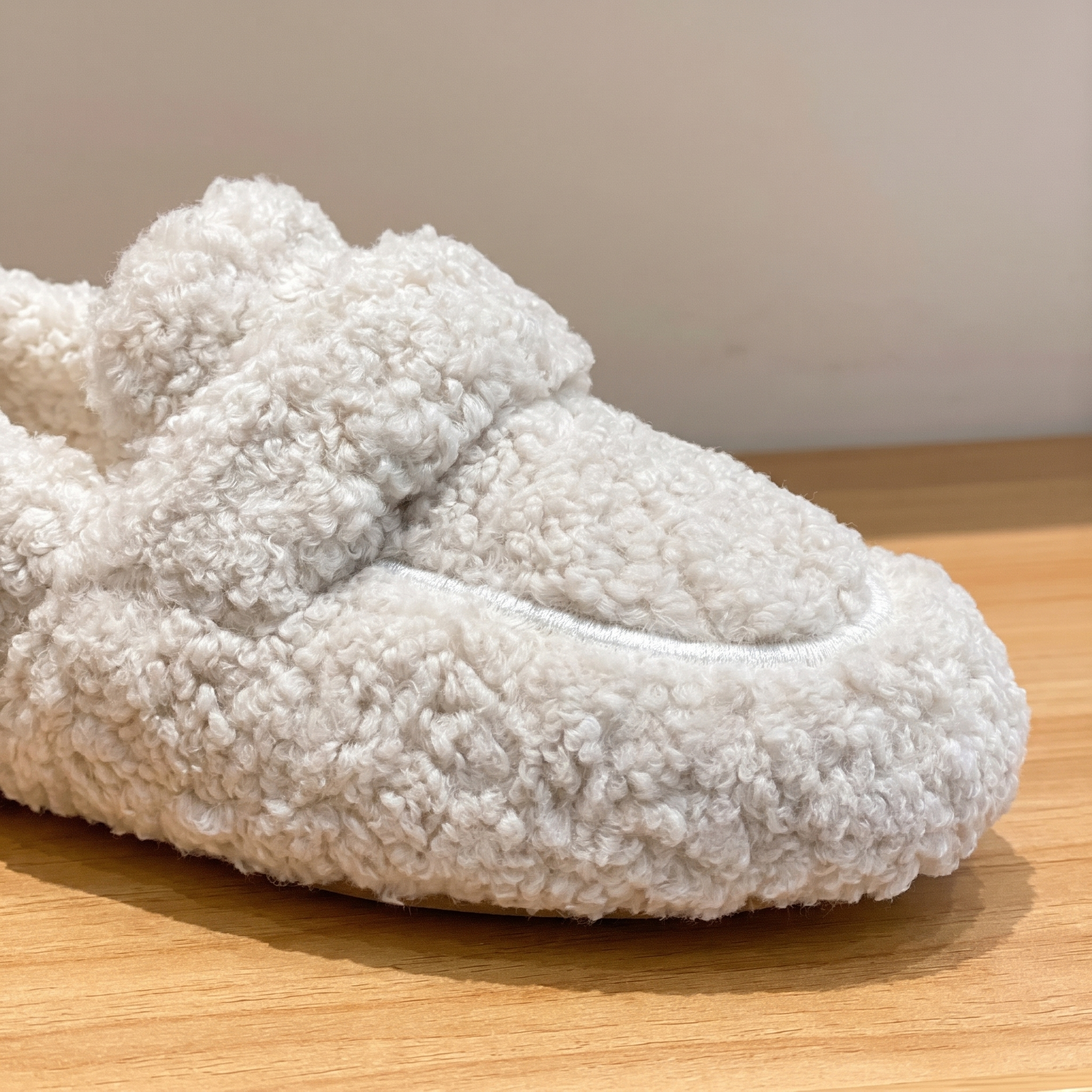 Beige plush teddy slipper close-up on a wood surface