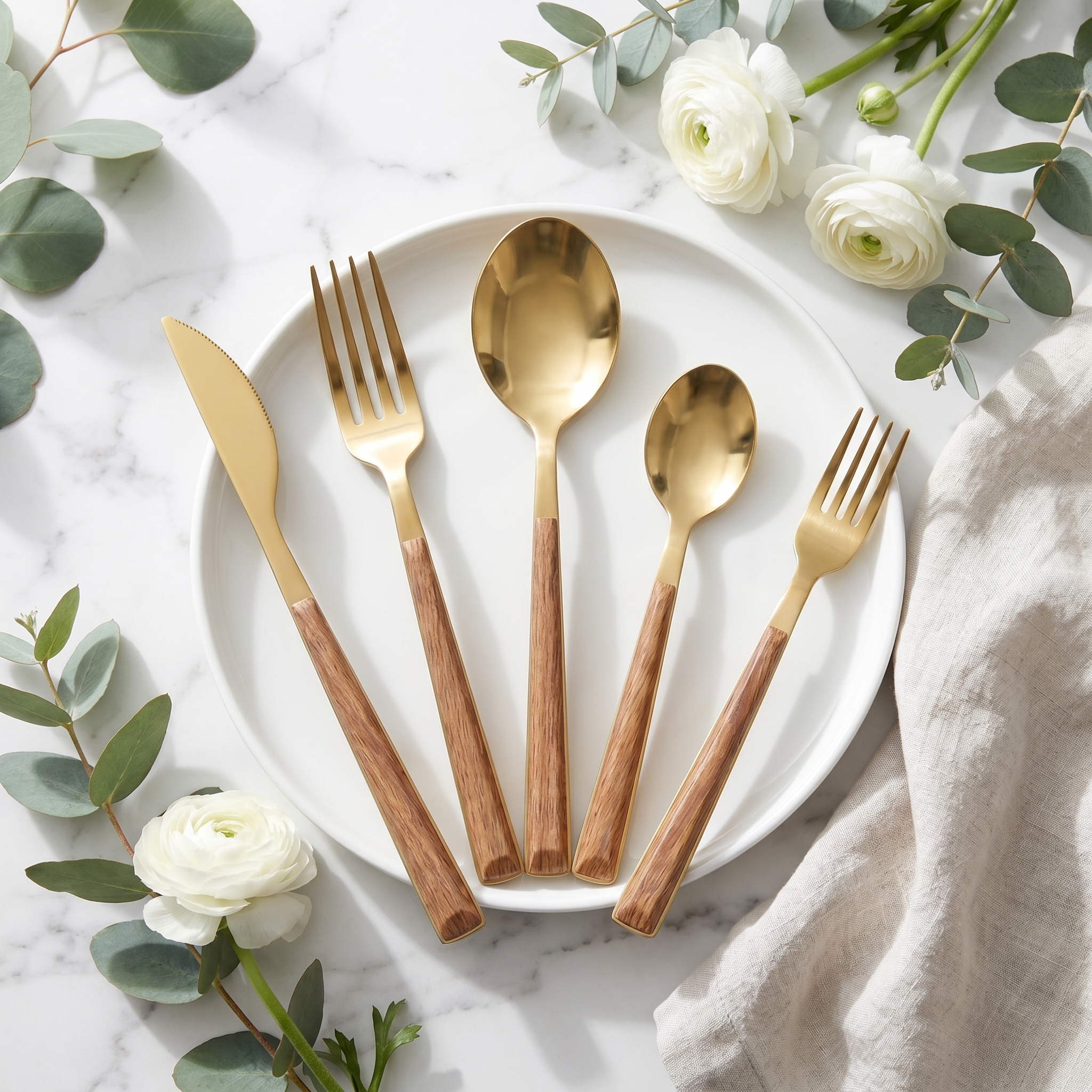 Gold wood-handle flatware flat lay with eucalyptus on marble