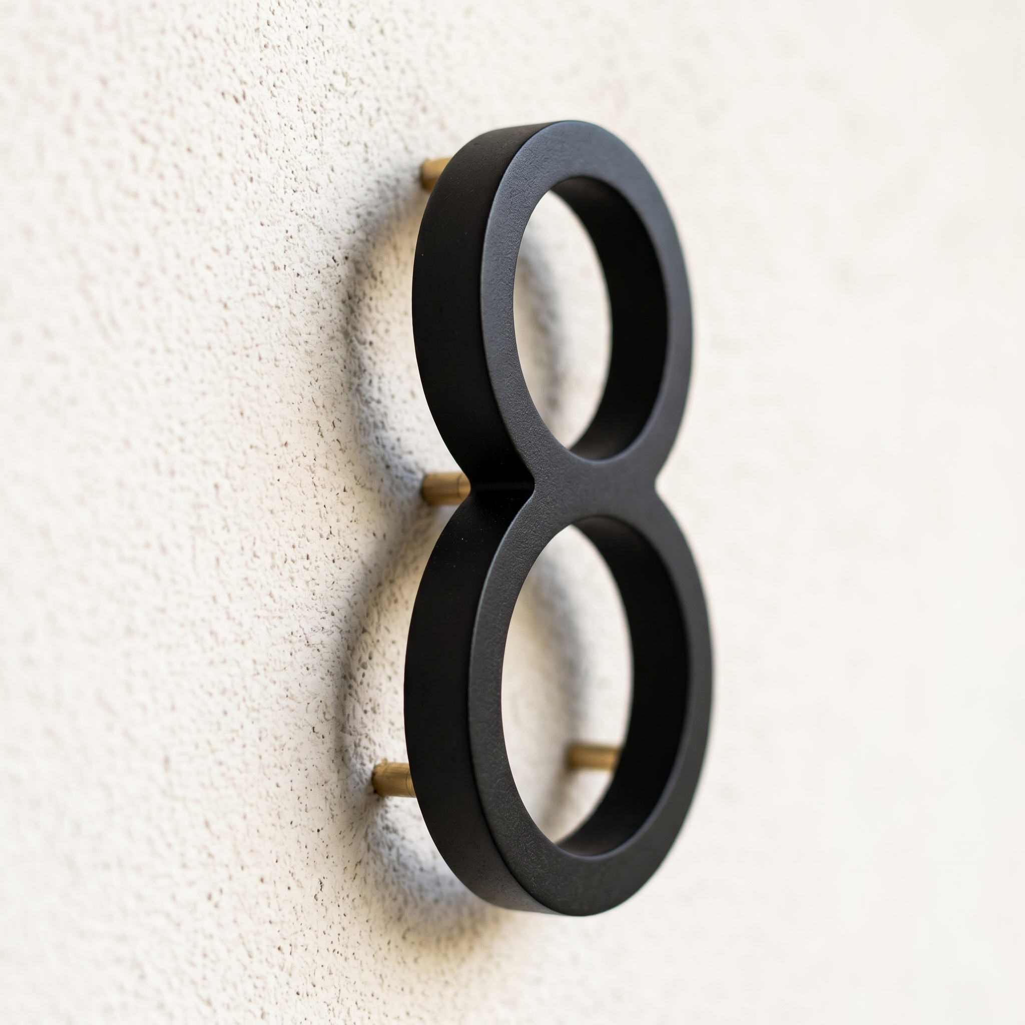 Close-up of a matte-black house number with float-mount standoff shadow