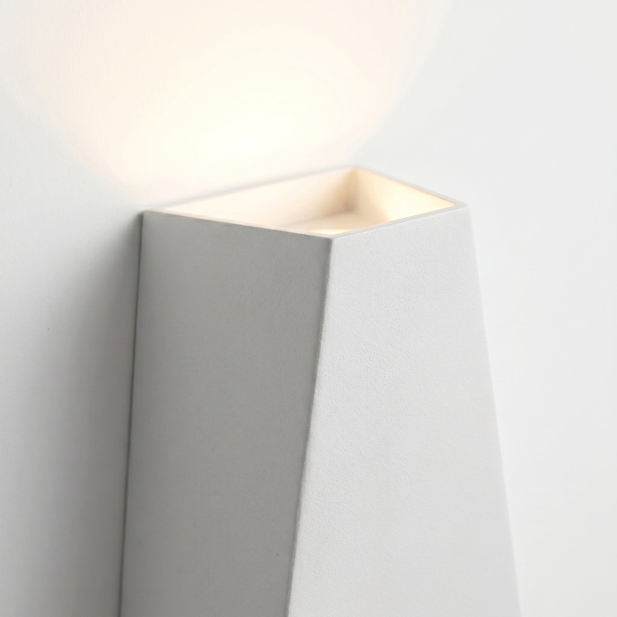 Macro detail of the Faccetta Aurora geometric wall sconce facet edges and warm glow