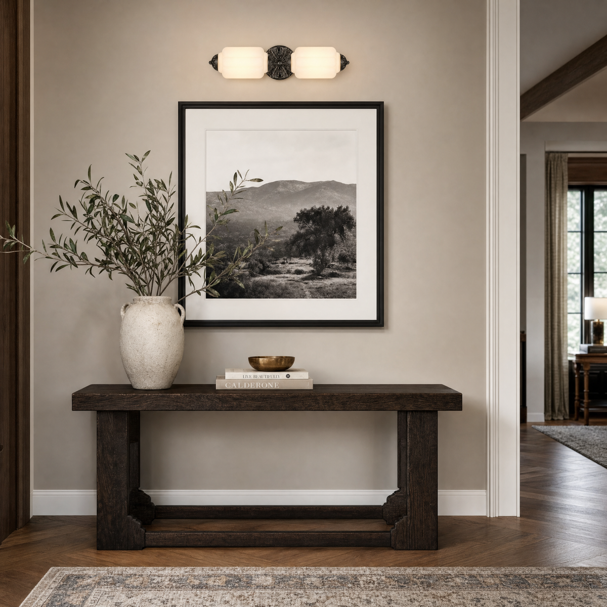 Frosted glass vanity light with black sunburst plate above framed artwork and an oak console in an entry hallway