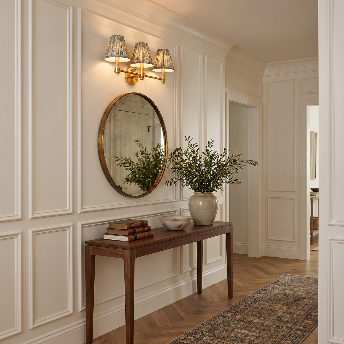 Terzetto brass wall sconce with green floral shades above a round mirror and walnut console in a hallway