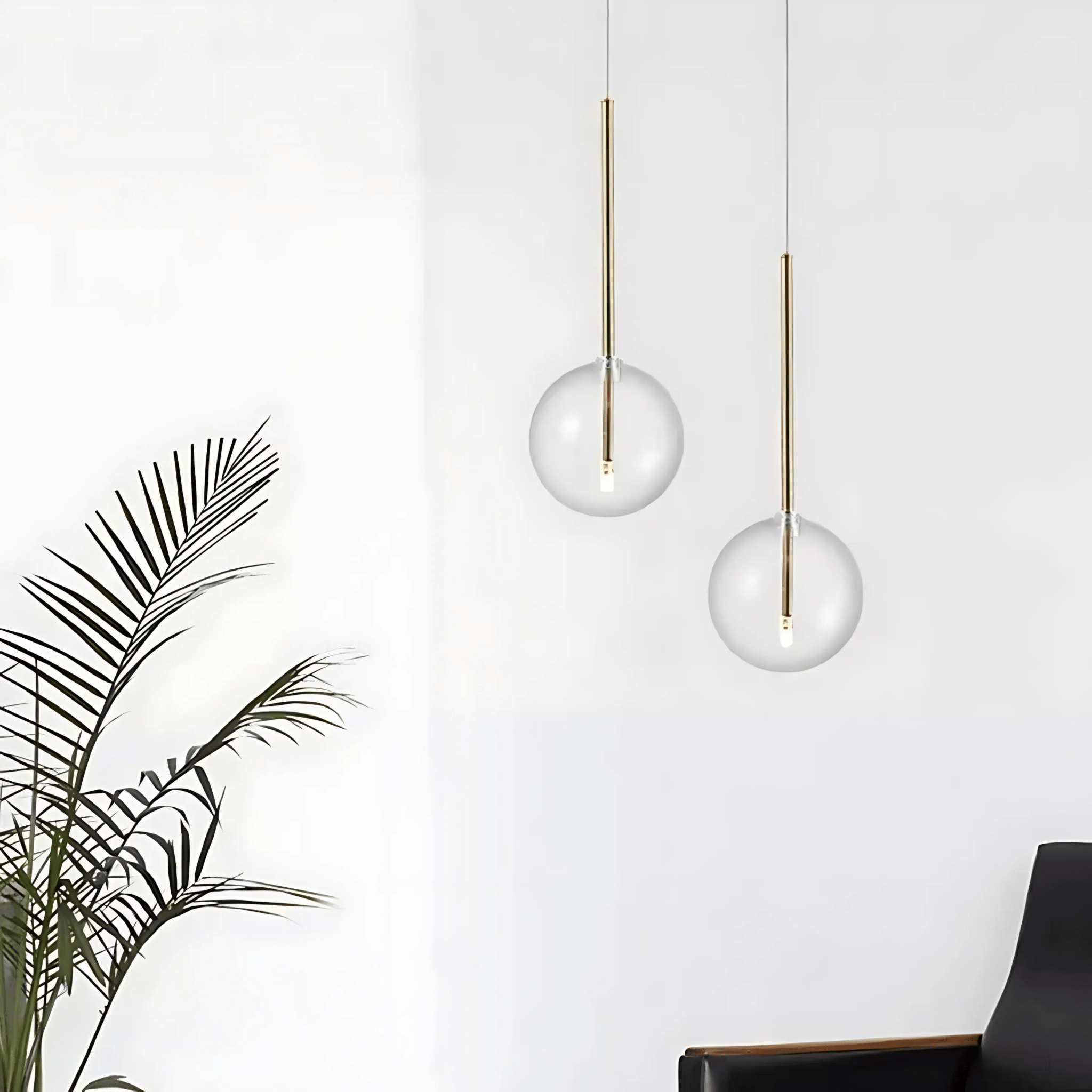 Two brass Goccia clear glass ball pendants glowing beside a leafy plant