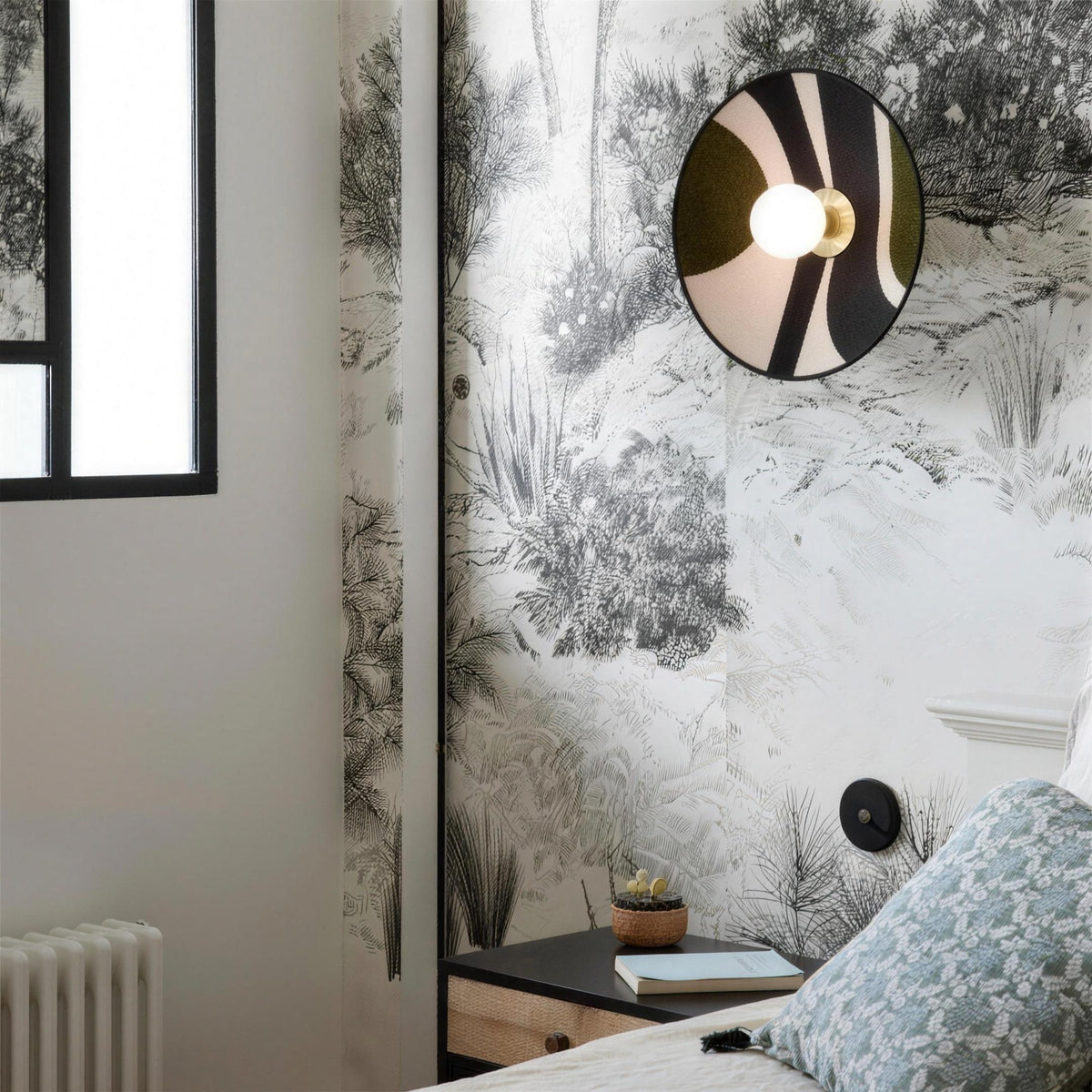 Luna Tessuta wall sconce in Forest Stripe beside a bed with toile wallpaper