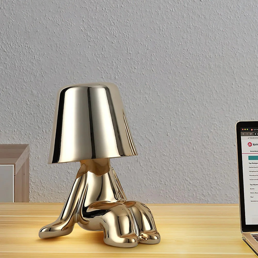 Gold sitting statue lamp on a wooden desk beside a laptop